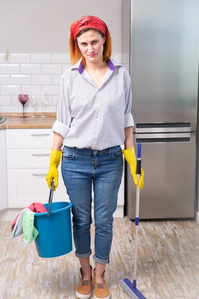 Изображение домохозяйки в защитных перчатках, держащей плоскую влажную швабру и ведро с тряпками во время уборки дома — стоковое фото