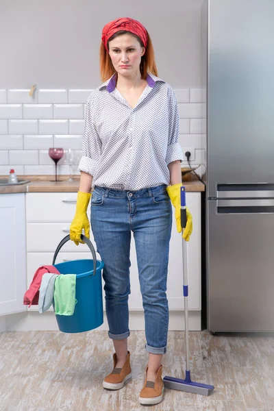 Jonge aantrekkelijke benadrukt service vrouw in wassen rubberen handschoenen dragen schoonmaak emmer-bezem en mop gefrustreerd en overwerkte op zoek vermoeid en lui — Stockfoto