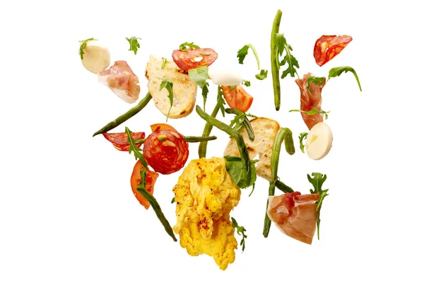 Geïsoleerde vallende groenten. Plakjes tomaat, ei, omelet, salami, ham, asperges, rucola en kaas. verse salade ingrediënten in de lucht geïsoleerd op witte achtergrond Stockfoto