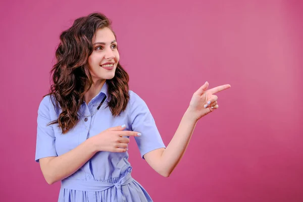 Retrato de mujer joven señalando las manos con el dedo en la esquina con copyspace sobre un fondo rosa —  Fotos de Stock