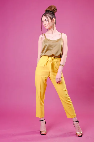 Young woman in yellow pants on pink background — 스톡 사진