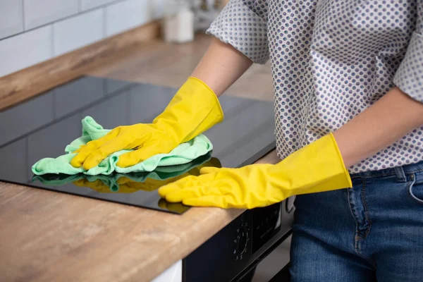 Kobieta sprzątająca blat indukcyjny, ręka w żółtej gumowej rękawiczce polerowana płyta grzewcza, zbliżenie, brak twarzy. przezroczyste urządzenie kuchenne — Zdjęcie stockowe