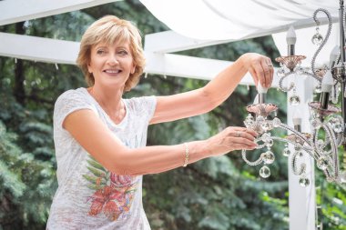 senior Woman changing a light bulb in a chandelier clipart