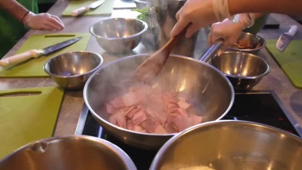 Close up of a slice of bacon fired in a cast-iron pan. Cook frying tiny slices of bacon on hot pan stirring them with a wooden spatula — Stock Video