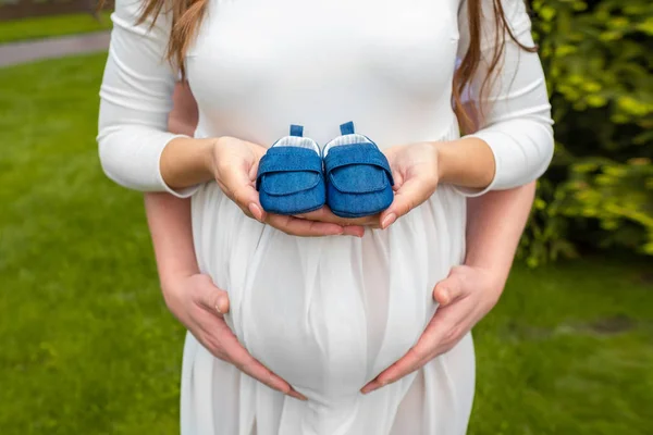 Close up loving couple with shoes for their baby. Gentleman hugging young pregnant woman from behind — Stock Photo, Image