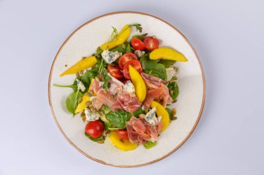 Salatayı jambonla karıştır, mavi peynir, domates, ayçekirdeği ve beyaz tabakta mango..