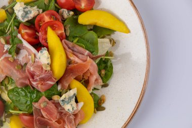 Salatayı jambonla karıştır, mavi peynir, domates, ayçekirdeği ve beyaz tabakta mango..