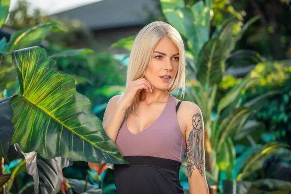 Retrato veraniego de moda de mujer sensual impresionante sexy, posando en un hotel de lujo cerca de plantas de la selva, usando ropa deportiva — Foto de Stock