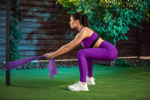 Ung kvinna tränar med gummiband utomhus. Friska aktiva livsstil koncept. flicka gör fitness i parken — Stockfoto