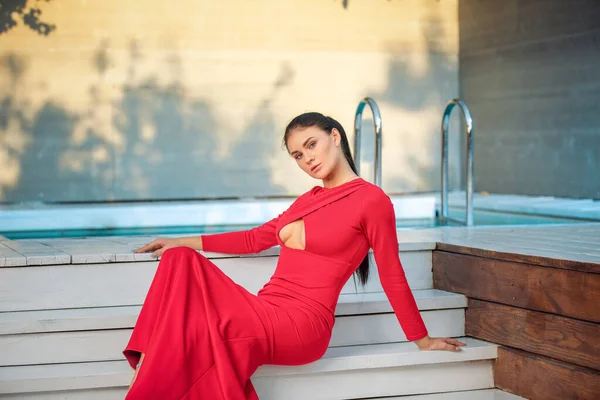 Mujer brinette moda en vestido largo rojo acostado junto a la piscina — Foto de Stock
