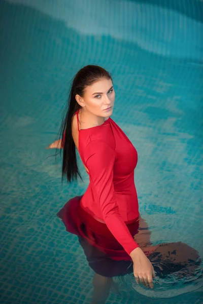 Young sexy woman floating on swimming pool in red dress. beauty shot