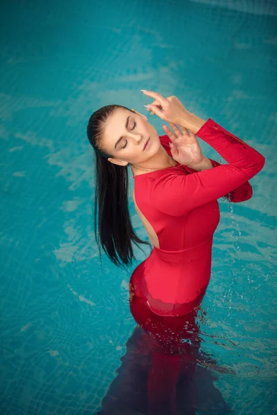 Young sexy woman floating on swimming pool in red dress. beauty shot