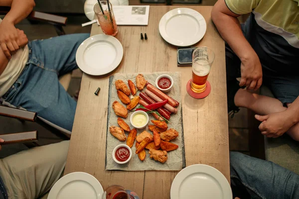 一緒に夕食を楽しむ 素朴な木製のテーブルに座っている間に一緒に夕食を持っている4人のトップビュー バーで軽食やクマを食べる男性のグループ — ストック写真