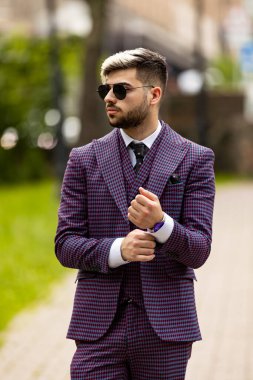 Genç ve çekici yönetici iş adamı menekşe gibi giyiniyor. Üç parçalı takım elbise dışarıda duruyor. Gömlek manşetlerini ayarlamak için giyiniyor.