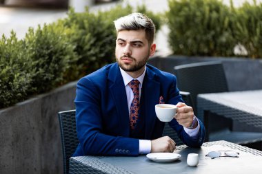 Düşünceli yakışıklı işadamı kafede kahve içip başka tarafa bakıyor.