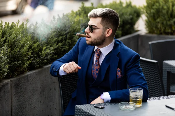 Stílusos jóképű férfi szivarozik és whiskyt iszik egy kávézóban. — Stock Fotó
