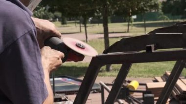 Erkek işçi, endüstriyel atölyede çalışırken açılı öğütücü kullanıyor. Metal keserken kıvılcımlar saçar