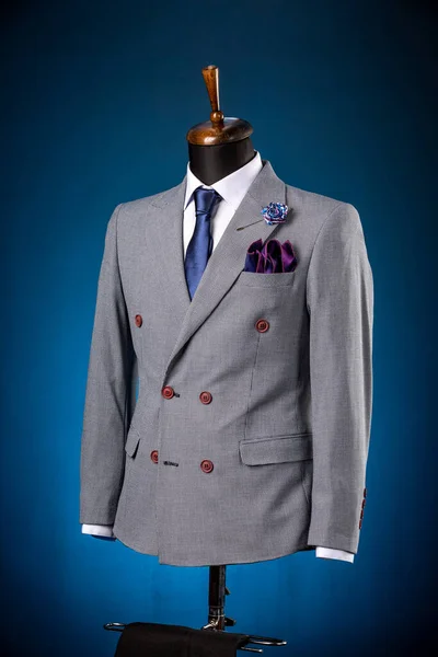 Beautiful men\'s grey jacket suit with shirt and tie on a dummy or mannequin on blue background. mens fashion for elegant men