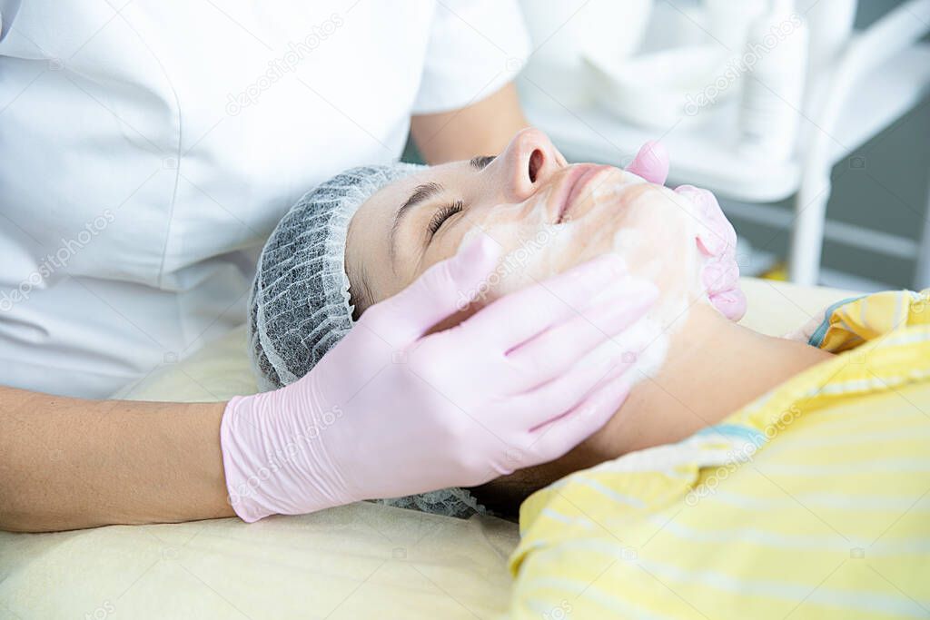 A close-up of the cleaning procedure in the office of cosmetology. Cleaning of the skin with foam. Woman in beauty salon on facial cleansing procedure. Cosmetologist's job. Close-up