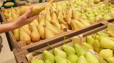 Dükkan penceresi. Marketin tezgahından alınmış meyveler. Kadın süpermarkette armut seçiyor.