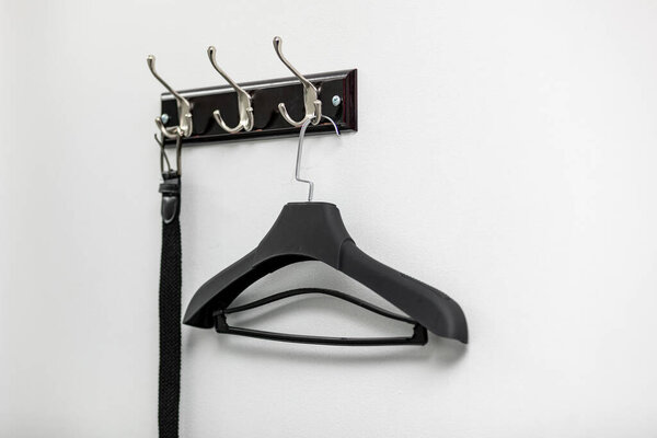 Male leather belt on hanger on hooks on light background.