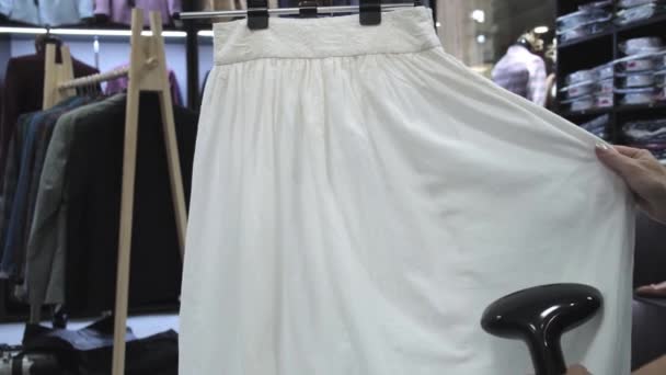 一个女人在服装店里蒸一条白裙子的侧视图。手持实时射击 — 图库视频影像