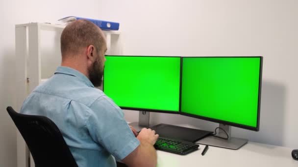 Wolny strzelec pracujący na komputerze, dwa monitory pokazują klucz Chroma. Zielony ekran i wyświetlacz arkusza kalkulacyjnego oprogramowania. mężczyzna piszący na klawiaturze w domu w izolacji i kwarantannie — Wideo stockowe