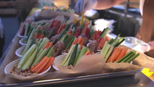 Салат в одноразових тарілках на фуршеті. офіціант готує Морква огірки кріп з соусом . — стокове відео