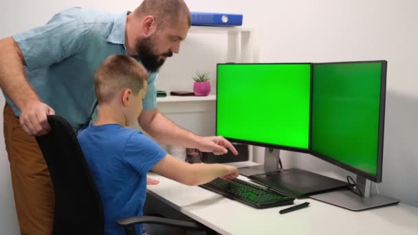 Πατέρας βοηθώντας ή διδάσκοντας το παιδί να πληκτρολογήσει στο πληκτρολόγιο εναντίον δύο πράσινων οθονών ή οθονών. εξ αποστάσεως μάθηση στο σπίτι υπό συνθήκες καραντίνας — Αρχείο Βίντεο