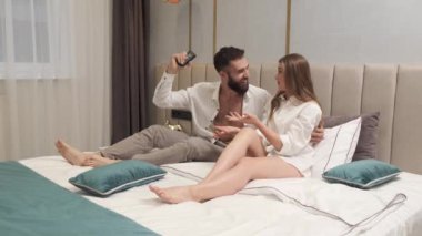 Yatakta uzanıp uzaktan kumandayla birlikte televizyon izleyen mutlu ve rahat bir aile çifti. Gülümseyen milenyum erkeği ve kadını konuşuyor. Yatak odasında televizyon seyrediyor..