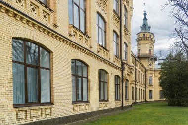 Kyiv. Kyiv Politeknik Enstitüsü. Geniş, sarı tuğla bina, detaylı mimari özelliklere sahip, sayısız pencere, ve bulutlu bir günde çevreleyen yeşil çimenler ve ağaçlar.