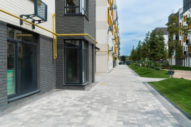 Güneşli bir günde iki modern konut binası arasında düzgün sıralanmış ağaçları ve fayanslı yüzeyi olan bir yaya geçidi.