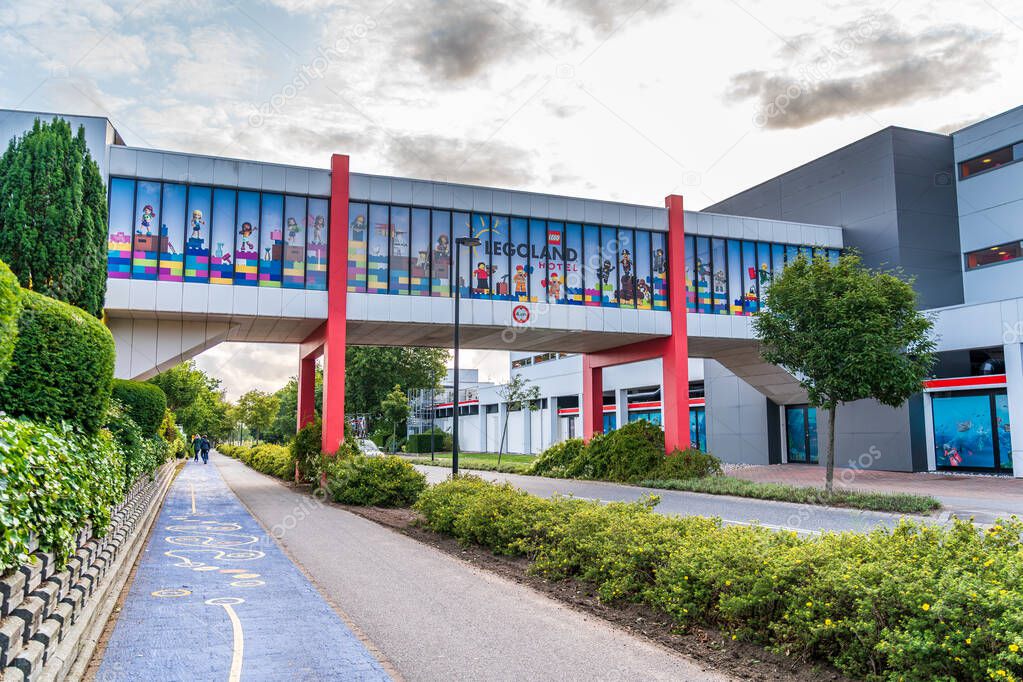 A vibrant covered bridge spans the road, pedestrian walkway and bicycle path, linking Legoland hotel with the theme park, adorned with colorful Lego figures and logo in Billund Denmark