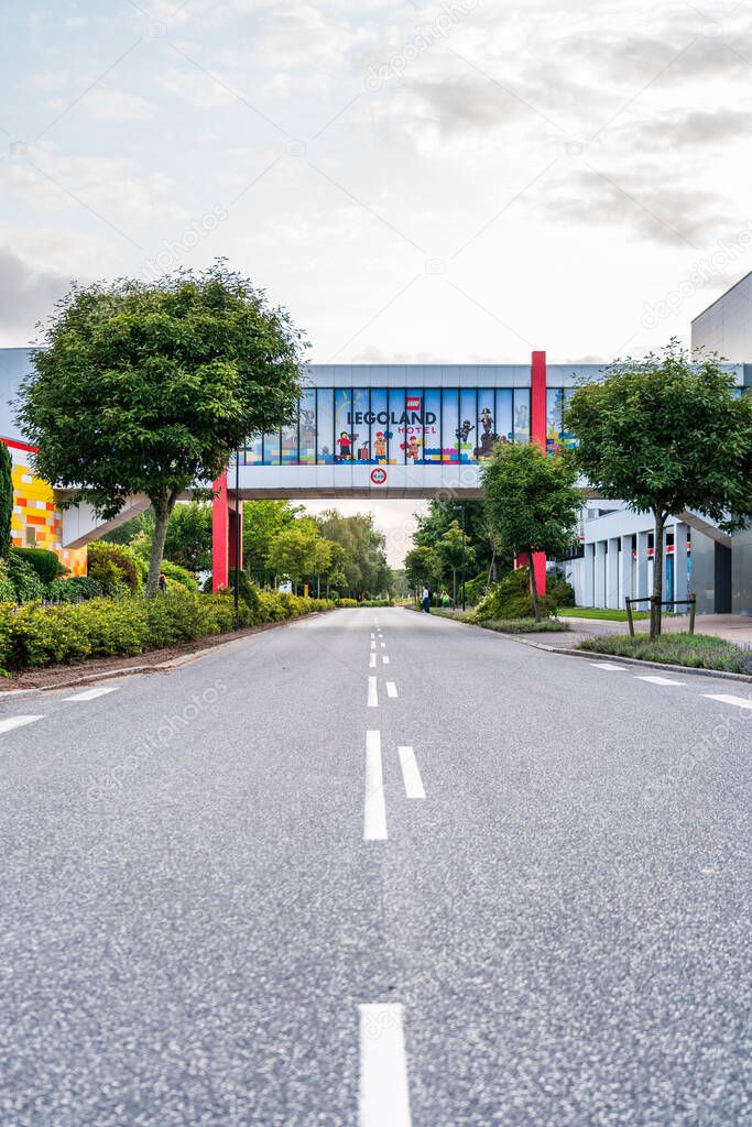 A road stretches beneath a covered bridge adorned with colorful posters. The bridge links Legoland Hotel and the theme park in Billund, Denmark, inviting visitors.