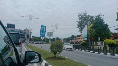 Trafik işaretleri, araçlar ve çevreleyen binalarla dolu bir yolu gösteren bir arabanın içinden alınan bir sokak görüntüsü..