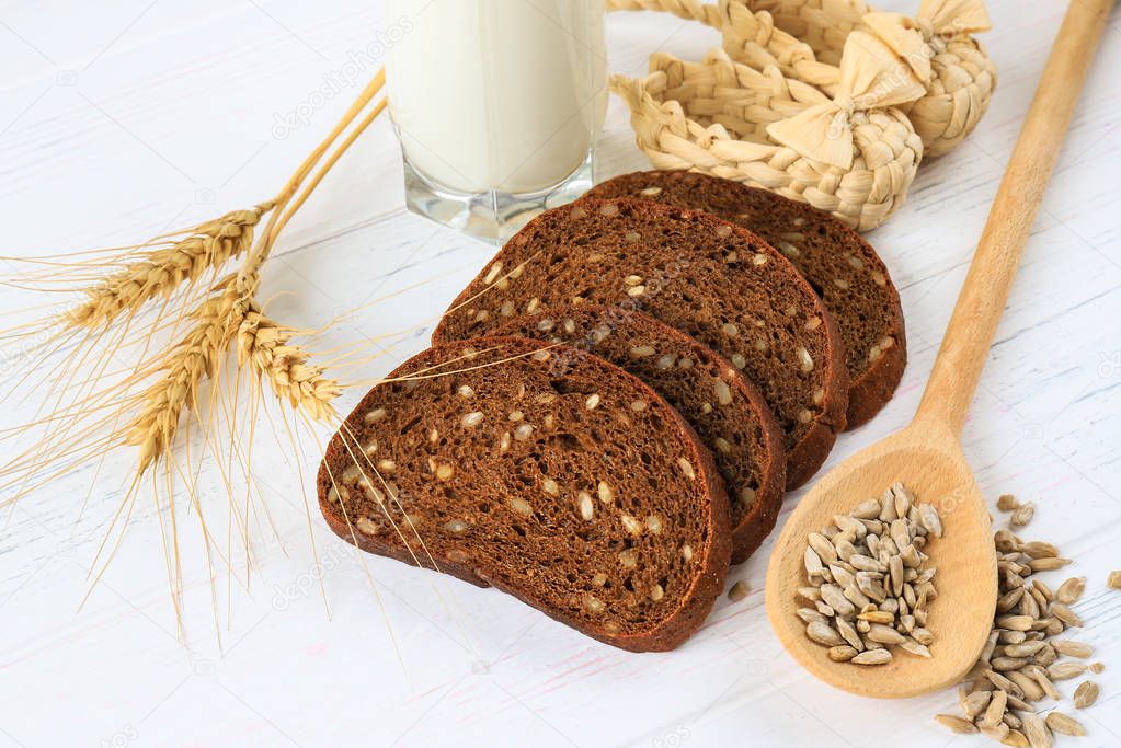 Rustic breakfast on a light wooden background - sliced bread, sunflower, seeds on a spoon, ears of wheat and a glass of milk