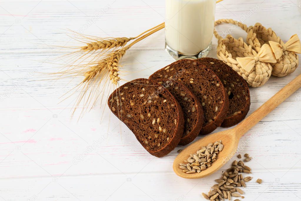 Rustic breakfast on a light wooden background - bread, sunflower, seeds on a spoon, spikelets of wheat and a glass of milk