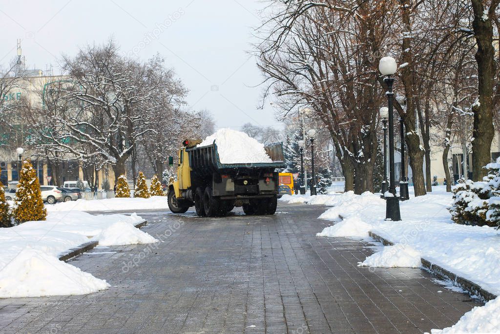 A large truck removes fresh snow from a snowy city street in winter. A big utility truck cleans the street in the cold season. Dnepropetrovsk, Ukraine