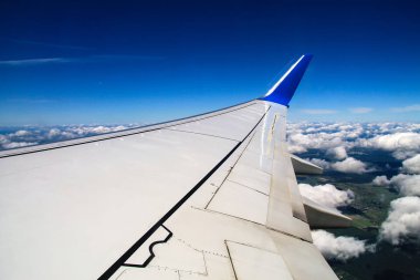 Mavi gökyüzünün arka planında uçağın kanadı ve güzel kümülüs bulutları. Bir uçak penceresinden bak.