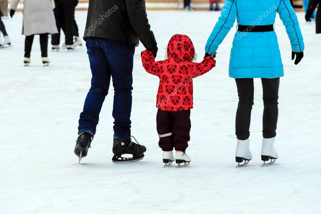 A little boy with his parents skates on the rink in the winter. Active family sport, winter holidays, sports clubs.