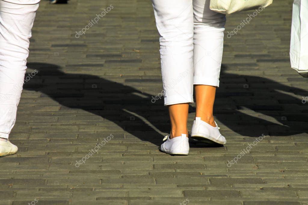 Female legs in white trousers and white shoes on a city street. Women at shopping and walking