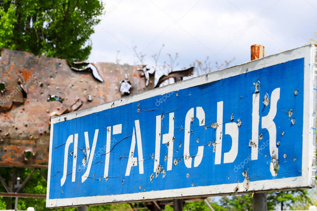 Blue road sign with the inscription in Ukrainian Lugansk, punched by bullets during the war in the Donbass, conflict East Ukraine, Ukrainian war