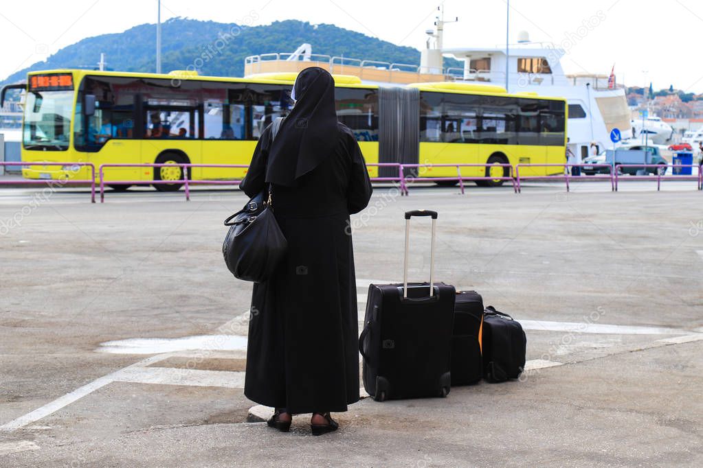 Nun traveling with suitcases and luggage. A woman in black monastic clothes is waiting for a bus on the waterfront of the old Croatian city Split. Travel, Croatia