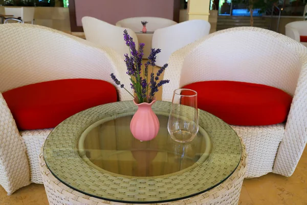 Rosa Vase mit einem Sommerstrauß Lavendelblüten auf einem Glastisch mit transparentem Glas vor dem Hintergrund eines weiß-roten eleganten Sessels — Stockfoto