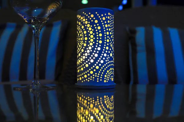 Lamp op de vakantie tafel in het avondeten. Elegante blauwe lantaarn met een gele kaars op een glazen tafel en een glas 's nachts. — Stockfoto