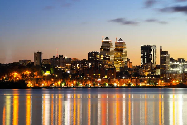 Torens, wolkenkrabbers, stadsgebouwen in de avond, lichten weerspiegeld op de rivier, grote stad nacht, zomer, lente, herfst. Dnipro Oekraïne, Dnepropetrovsk — Stockfoto