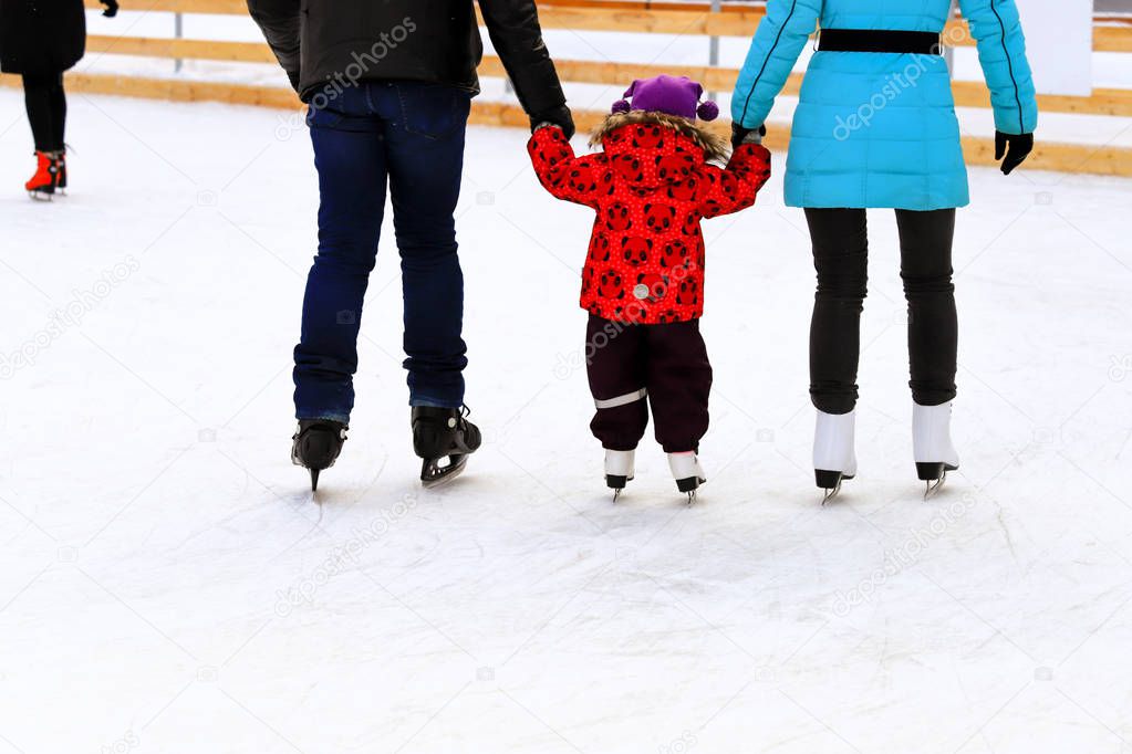 A l boy with dad and mom skates on the rink in the winter. Active family sport, winter holidays, sports clubs.
