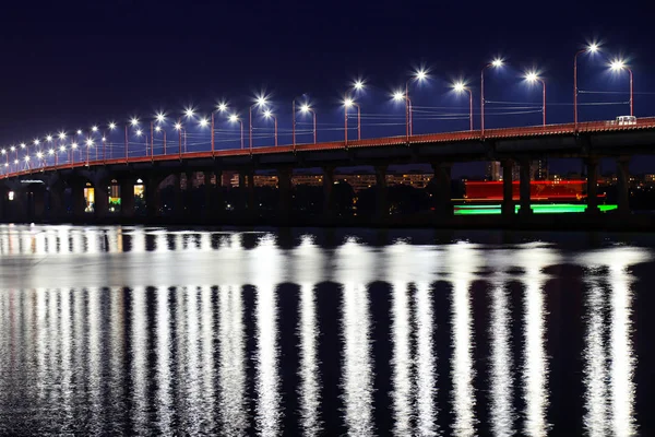 Noční most s nádherními lampióny se odráží ve vodě na řece Dnieper, ve městě Dnepropetrovsk, na Ukrajině. Večerní řeka ve velkém městě. — Stock fotografie
