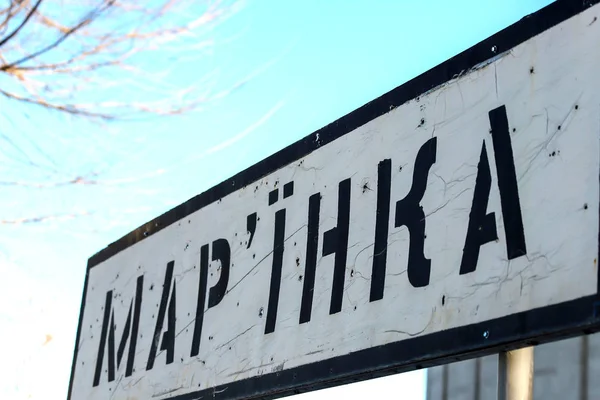 Verkeersbord met de inscriptie in het Oekraïens-Marinka, regio Donetsk, gebroken door kogels tijdens de oorlog in de Donbass, Oekraïne. Gewapende conflict ten oosten van Oekraïne, vernietiging in ATO. — Stockfoto