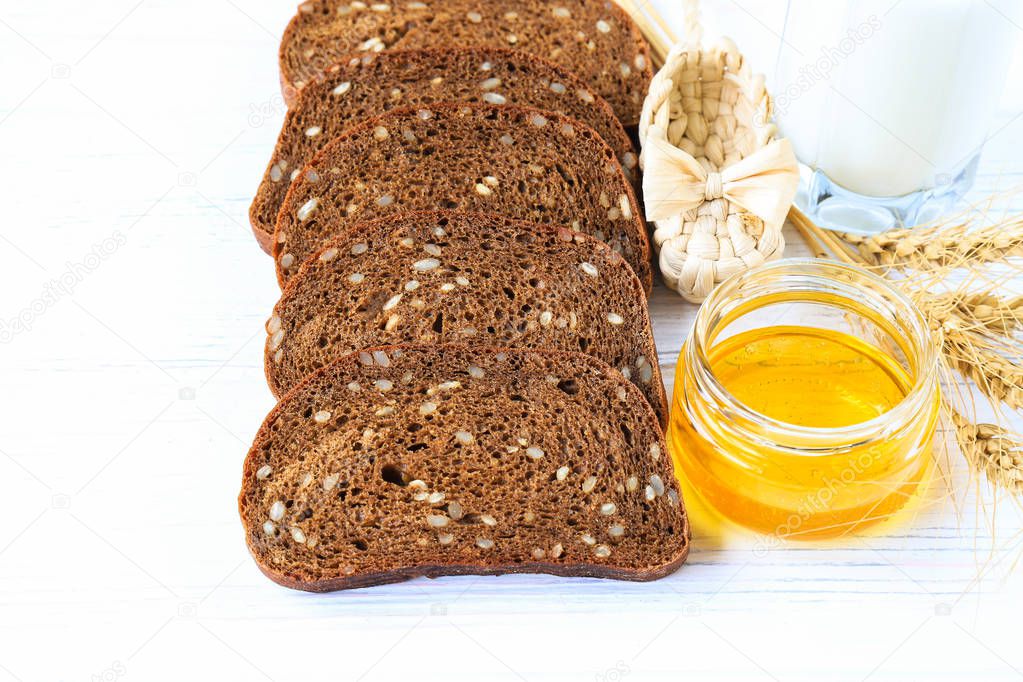 Rustic breakfast on a light wooden background - sliced bread with seeds, ears of wheat. straw wicker shoes. cup with honey